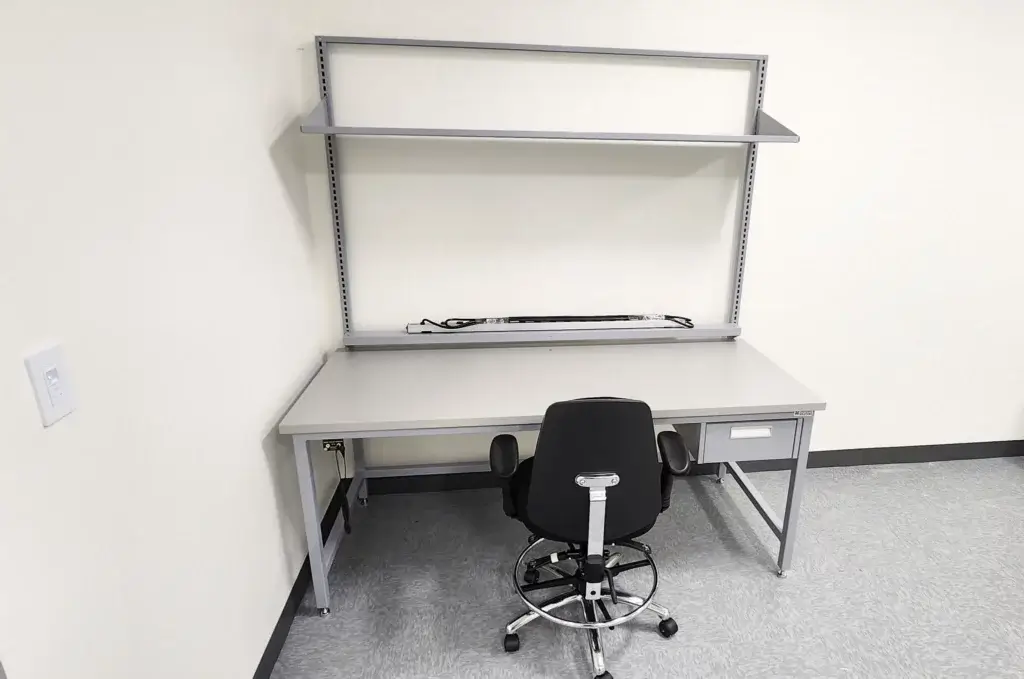 Light grey ESD workbench with power strip and overhead shelving.