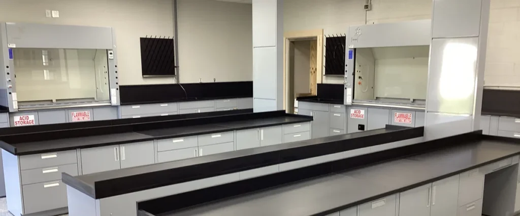 OnePointe Solutions painted steel lab casework with twin fume hoods, ACID STORAGE and FLAMMABLE base cabinets, and black epoxy island workstations